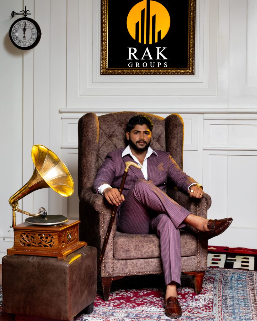 Corporate portrait of the RAK Groups owner sitting confidently in a winged armchair, dressed in a mauve suit with an open-collar shirt and holding a walking cane, beside a vintage gramophone.