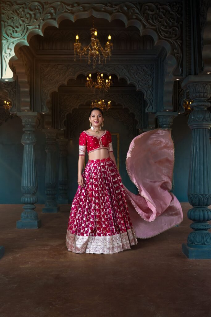 Actress in a Shreevaraa Designs hot pink lehenga choli with flowing dupatta and heavy gold embroidery, posing majestically in a grand, dimly lit, traditional Indian palace interior.
