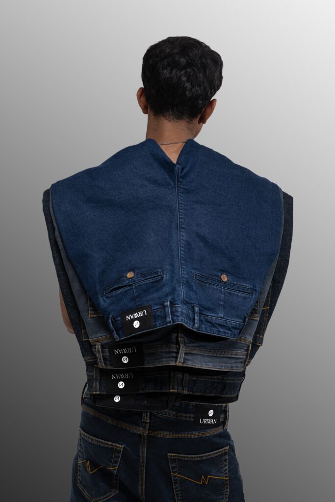 A male model photographed from behind wearing multiple layers of denim jackets stacked on his shoulders, styled creatively for a fashion editorial shoot.