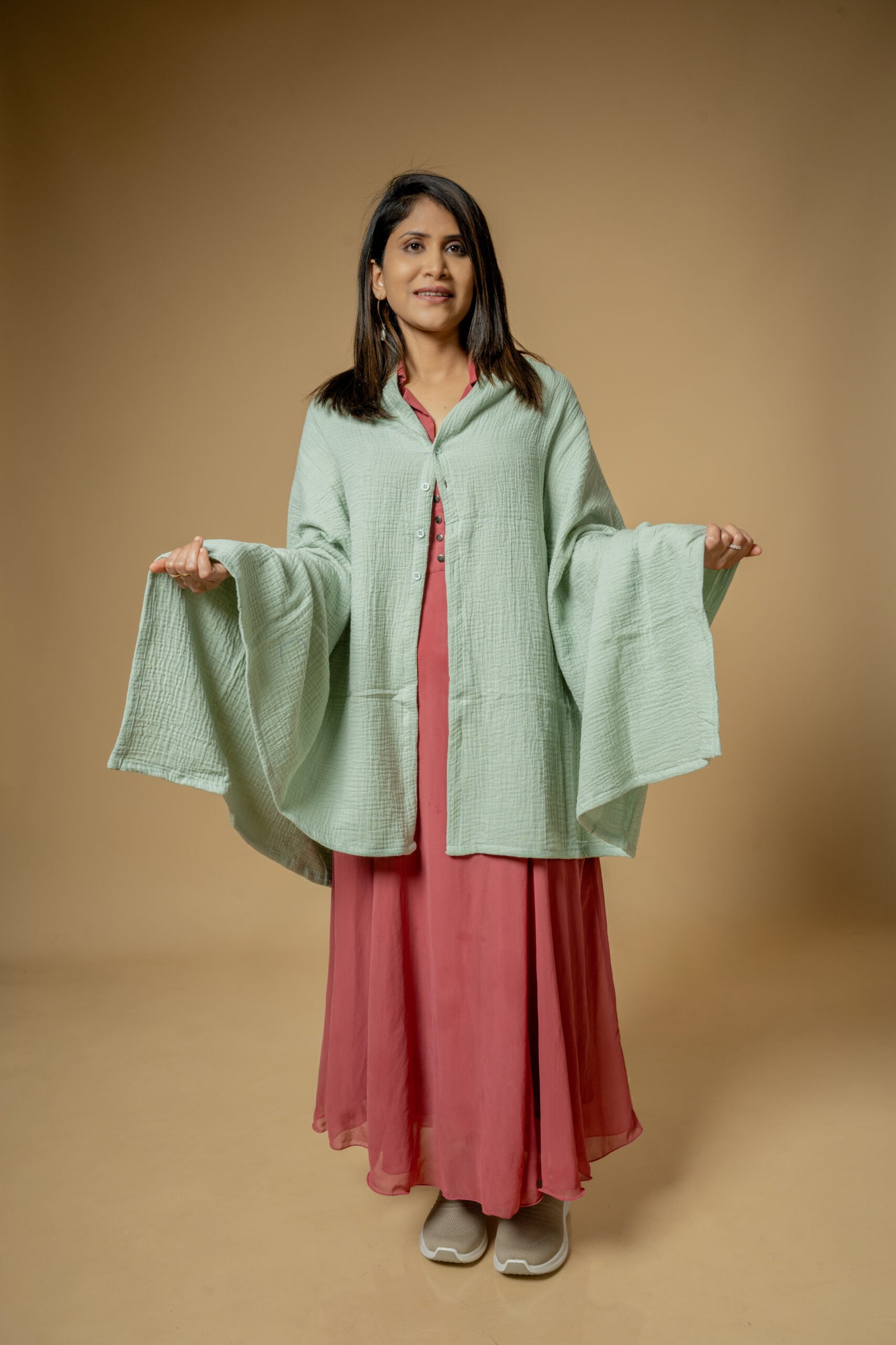 Model showcasing a sage green poncho over a pink dress during a catalogue shoot by UrbanPixelites